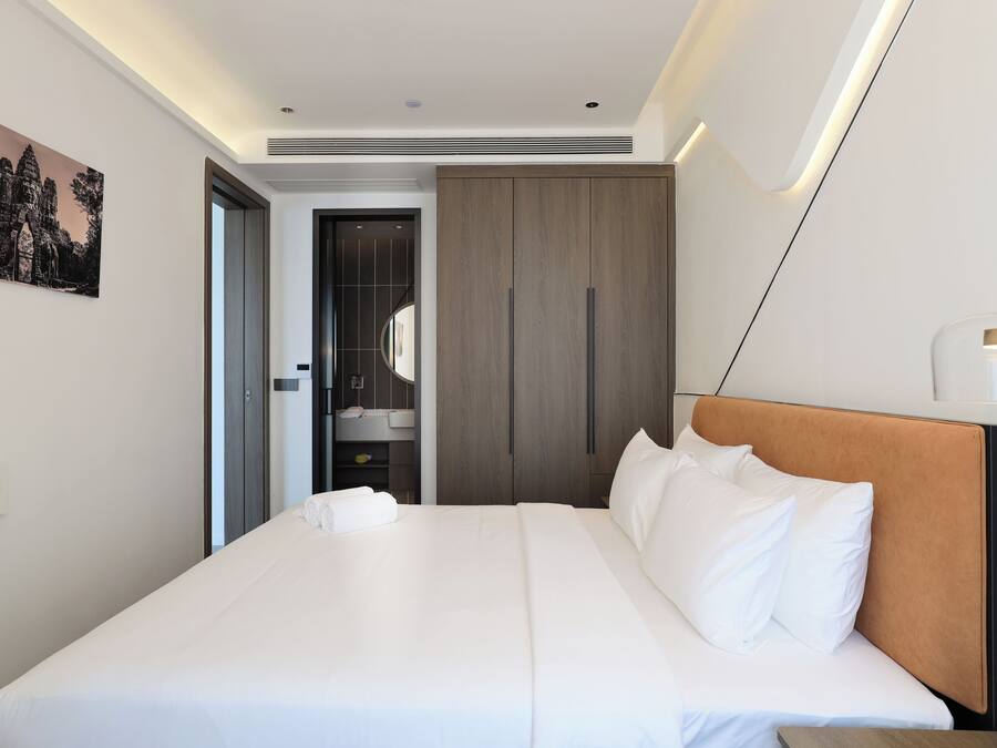 Habitación de hotel moderna con una cama grande, un armario de madera y un baño visible a través de una puerta abierta.