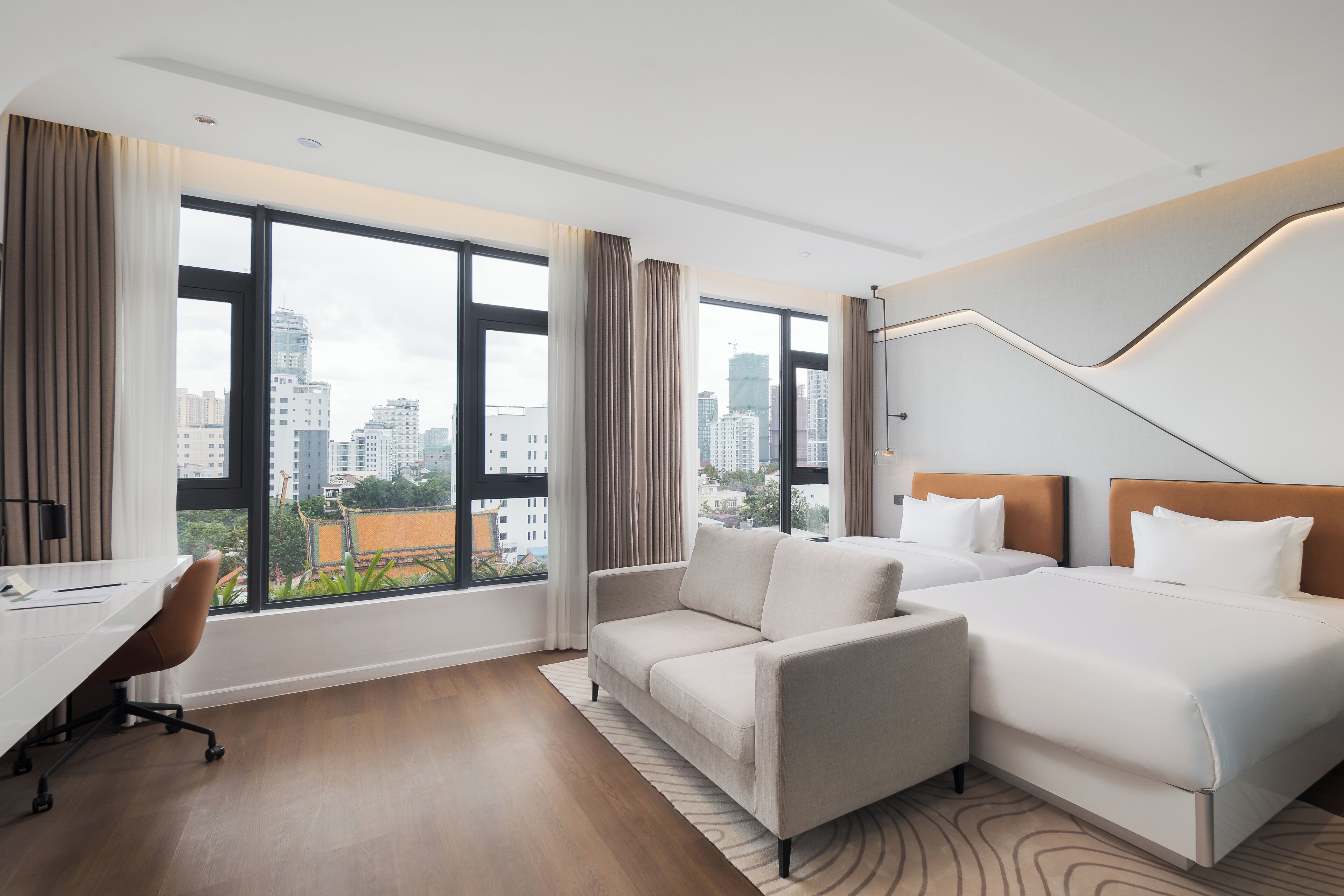 Una habitación de hotel moderna con un ventanal grande, un sofá, una cama y un escritorio.