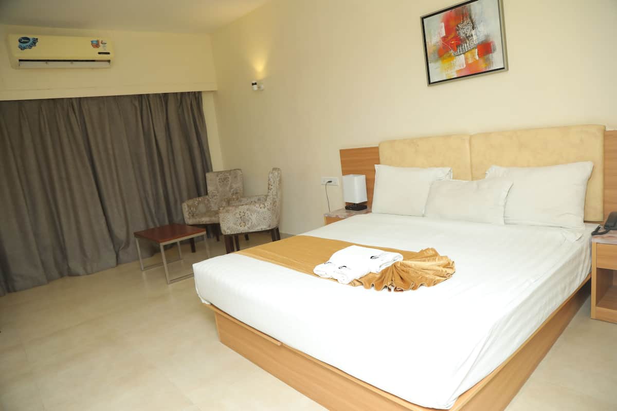 A hotel room with a large bed, a chair, a desk, and an air conditioning unit.