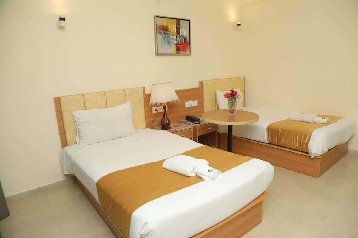 A hotel room with two beds, a small table, a lamp, and a painting on the wall.