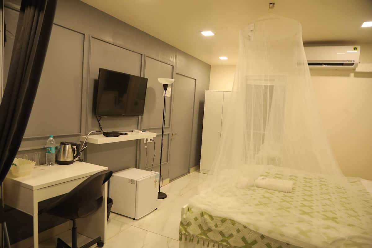 A hotel room with a bed, a desk, a television, a small refrigerator, and an air conditioning unit.