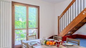 Un coin repas avec une table dressée pour deux personnes, une bouilloire rouge et un panier de fruits.