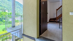 Une pièce dotée d’une porte en bois, d’un balcon avec une rambarde en métal et offrant une vue sur une colline verdoyante.