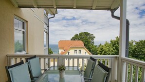 A balcony with a glass table and chairs, overlooking a coastal view with a house in the background. - Fantastic sea view from the balcony, use of swimming pool and sauna - Villa Bergfrieden (Göhren)