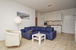 A modern living room with a blue sofa, a white armchair, and a small white coffee table.