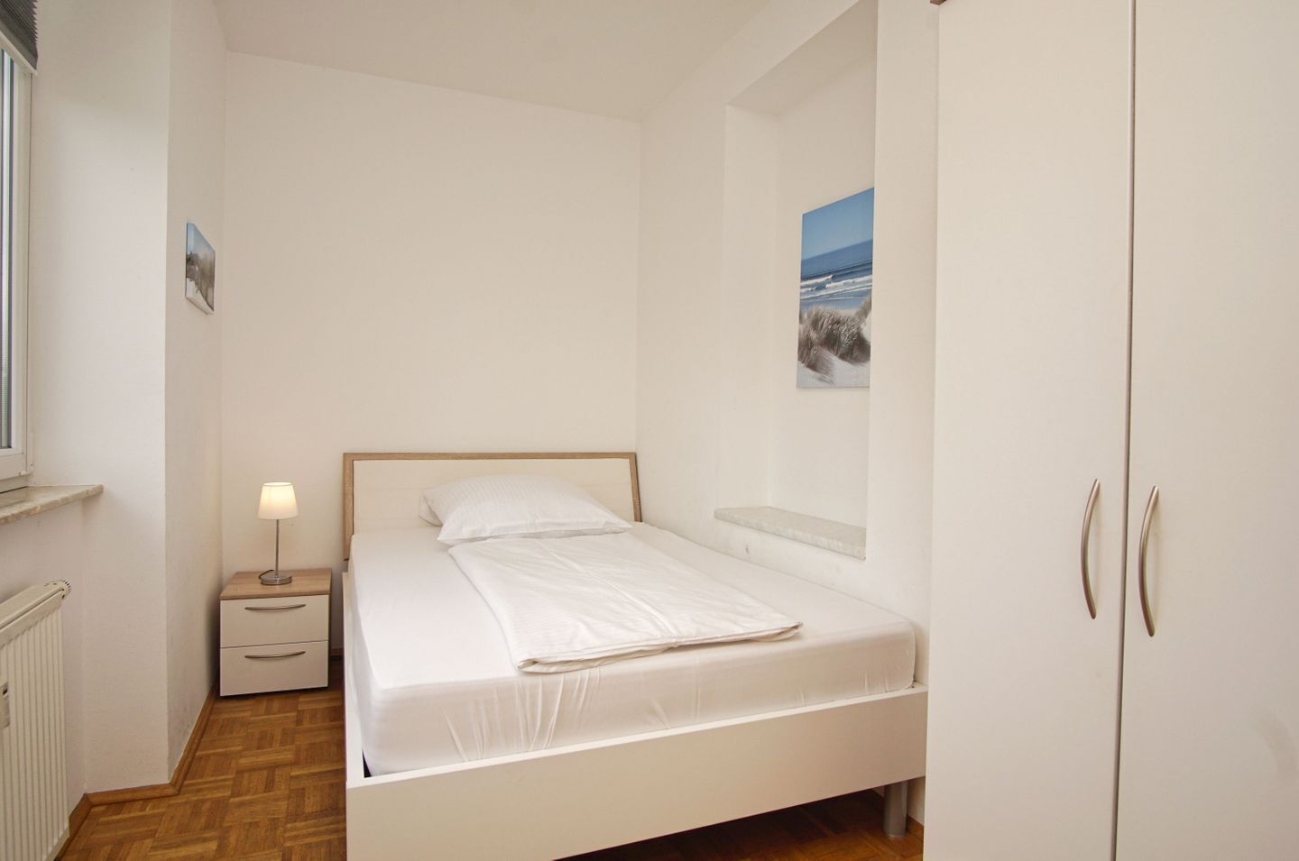 A bedroom with a single bed, a nightstand with a lamp, a radiator, and a wardrobe.