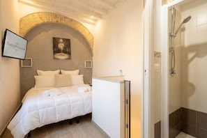 Une chambre à coucher comprenant un lit, une table de chevet, une armoire, une douche et un tableau encadré accroché au mur.