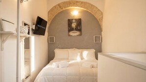 A bedroom with a bed, a TV, a painting, and a stone archway.