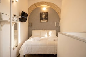 A bedroom with a bed, a TV, a painting, and a stone archway.