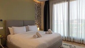 Een hotelkamer met een groot bed, een nachtkastje, een lamp en dunne gordijnen.