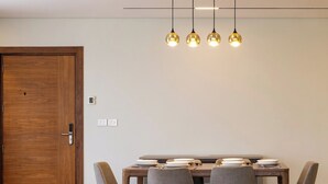 Een eethoek met een houten tafel, vier grijze stoelen en een hanglamp met vier lampjes.