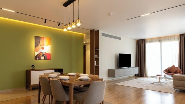 Een moderne woonkamer met een eethoek, een flatscreen-tv en een groot raam met gordijnen.