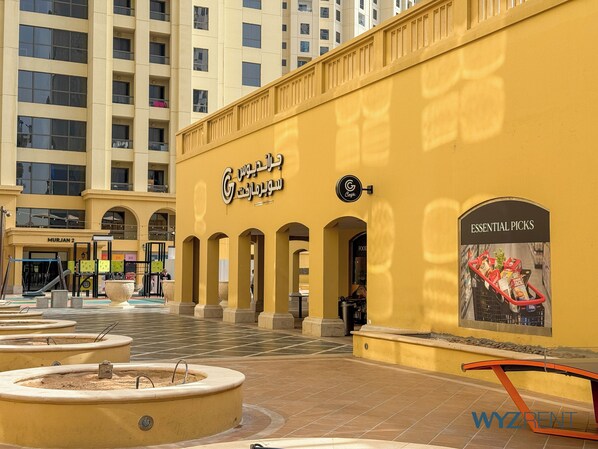 A yellow building with a sign reading "G Coffee" and "ESSENTIAL PICKS" on the right. There are multiple arches and a playground with slides in the foreground.