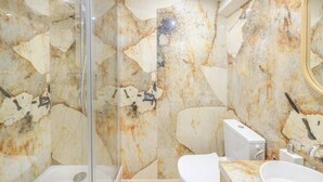 A bathroom with marble walls, a glass shower enclosure, a white toilet, and a sink with a mirror. - Apartment Como - Villa Alcôme (Paris)