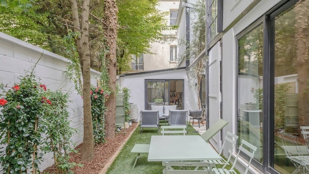 A modern outdoor patio with a table and chairs, surrounded by greenery and a white wall. - Apartment Como - Villa Alcôme (Paris)