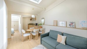 A modern living room with a sofa, a dining table, and chairs. There is a kitchen area with a sink and a mirror. The room has a skylight and a view of the city. - Apartment Como - Villa Alcôme (Paris)