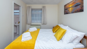 A hotel room with a bed, a painting, a window with curtains, and a bathroom visible through an open door. - Nant Y Mynydd (Amlwch)