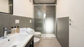 A modern bathroom with a glass-enclosed shower, a white sink, and toiletries. - Dimora dei Colori - Yellow Light (Bari)
