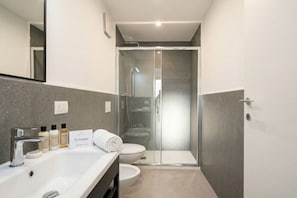 A modern bathroom with a glass-enclosed shower, a white sink, and toiletries.