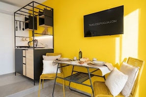 A compact kitchen with a dining area, a TV mounted on the wall, and a yellow wall. - Dimora dei Colori - Yellow Light (Bari)