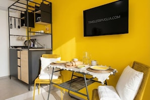 A bright yellow room with a dining table set, a kitchen area with utensils, and a framed sign on the wall.