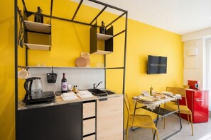 A compact kitchen with a black countertop, a wine bottle, and a kettle.