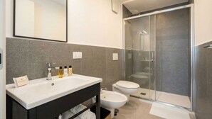 Een moderne badkamer met een grote spiegel, een witte wastafel, een toiletbril en een douche met glazen wanden.