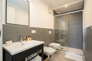 Et moderne badeværelse med et stort spejl, en hvid vask, en bidet og en brusekabine med glasvægge.