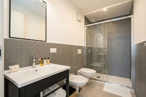 A modern bathroom with a large mirror, a white sink, a bidet, and a glass-enclosed shower. - Dimora dei Colori - Yellow Light (Bari)