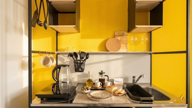 A compact kitchen with a yellow backsplash, a coffee maker, a kettle, a bread loaf, and a wine glass on the counter. - Dimora dei Colori - Yellow Light (Bari)