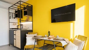 Een kleine keuken met een eethoek, een aan de muur bevestigde televisie en een gele wand.