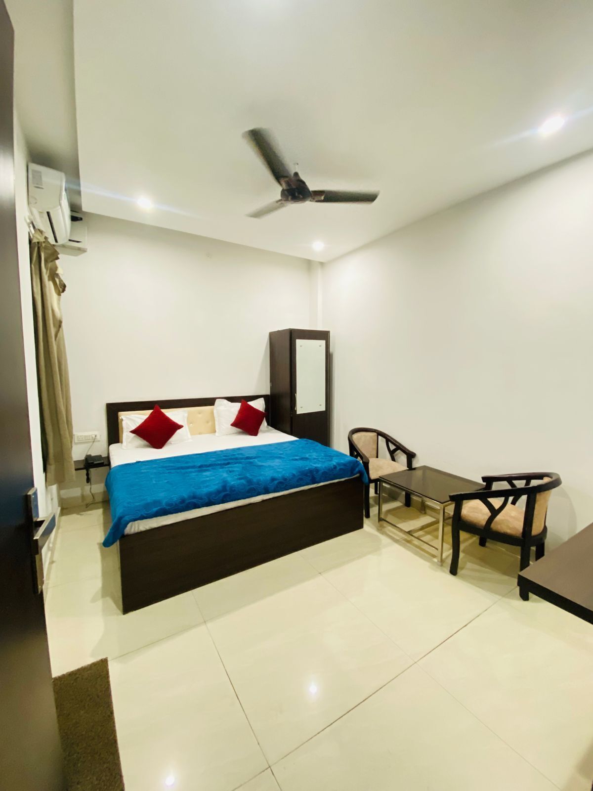 Une chambre d’hôtel équipée d’un lit, d’un bureau, d’une chaise, d’un ventilateur de plafond et d’un miroir.