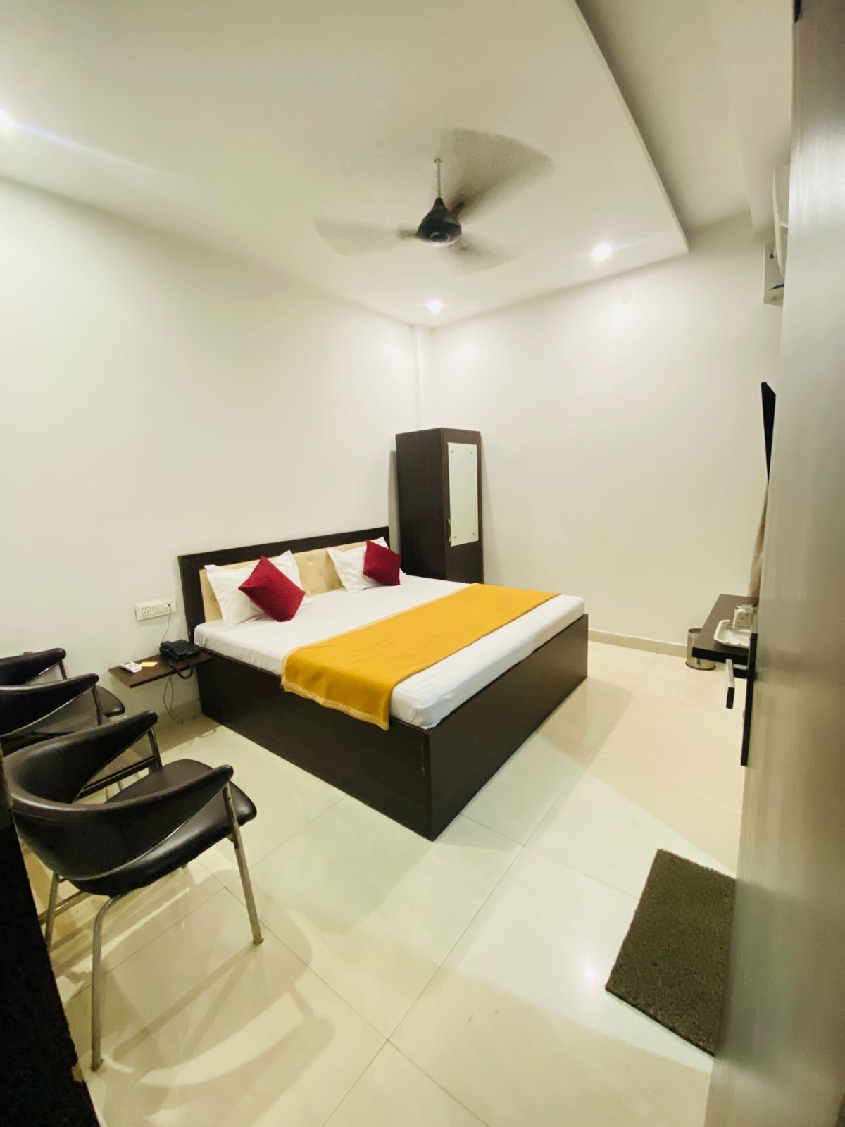 A modern hotel room with a bed, a desk, a chair, a wardrobe, and a ceiling fan.