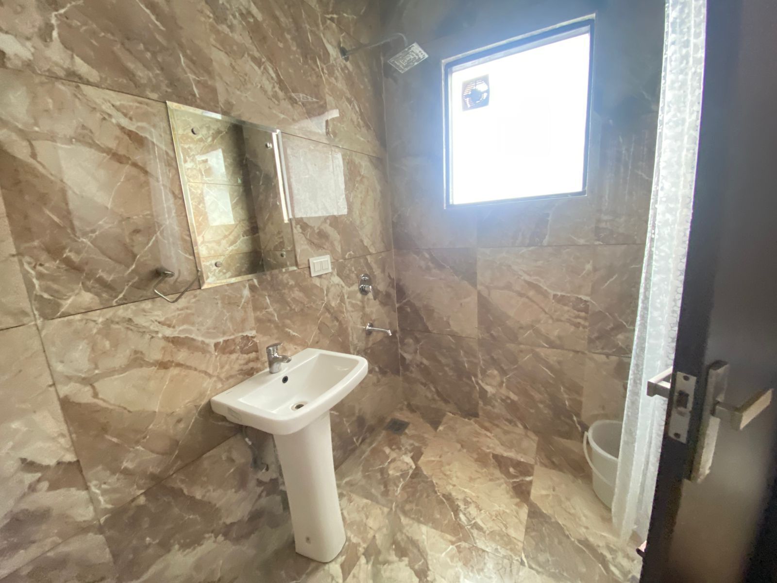 A bathroom with a marble floor, a white sink, a mirror, and a window.