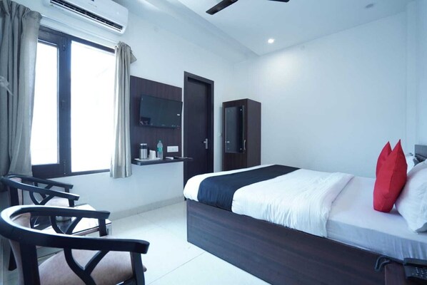 A modern hotel room with a large bed, a desk, and a chair. There is a window with curtains, a mirror, and a wardrobe.