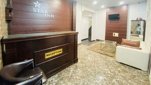 A hotel reception area with a reception desk, a reception sign, a sofa, a TV mounted on the wall, and a ceiling fan. - Hotel Star Karnal (Karnal)
