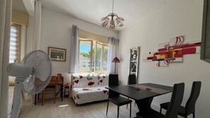 A dining area with a table and chairs, a sofa with a floral pattern, a fan, and a ceiling light fixture. - GuestHost - Villa Augusta (Cervia)