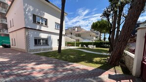 A modern two-story building with a paved courtyard, a covered seating area, and a well-maintained lawn. - GuestHost - Villa Augusta (Cervia)
