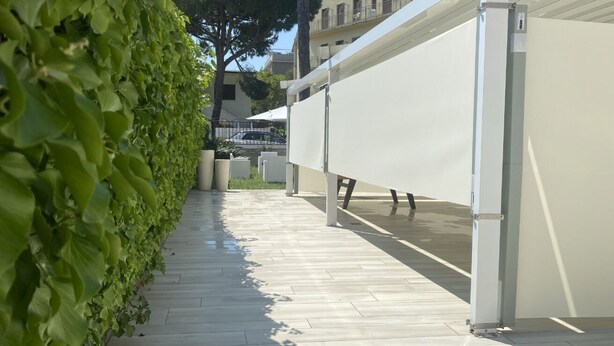 A corridor with a green hedge, a tiled floor, and a white structure with a flat surface. - GuestHost - Villa Augusta (Cervia)