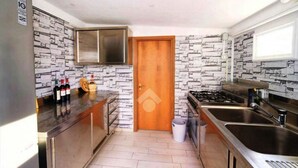 A kitchen with a stone backsplash, stainless steel appliances, and a wooden door. - GuestHost - Villa Augusta (Cervia)