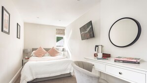 Een slaapkamer met een bed, nachtkastje, stoel, kapstok en een spiegel, plus een raam.