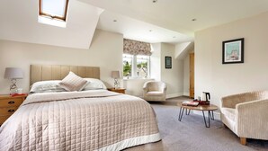 Une chambre à coucher avec un grand lit, une chaise, une petite table et une fenêtre donnant sur l’extérieur.