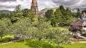 A church with a tall spire, surrounded by lush greenery and a park with benches and playground equipment. - Kelsick Villa Guest House - Wansfell (Ambleside)