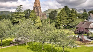 A church with a tall spire, surrounded by lush greenery and a park with benches and playground equipment.