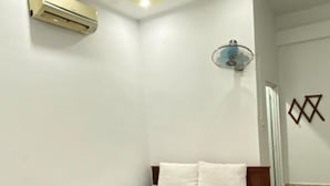 A bedroom with a wooden bed, white bedding, an air conditioner, a wall-mounted light fixture, and a geometric wall decoration. - Sugar Motel (Can Tho)