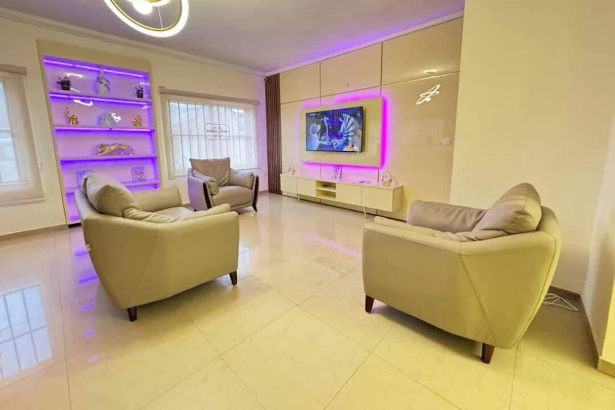 Una sala de estar moderna con dos sofás beige, un televisor de pantalla plana y una estantería empotrada con objetos decorativos.
