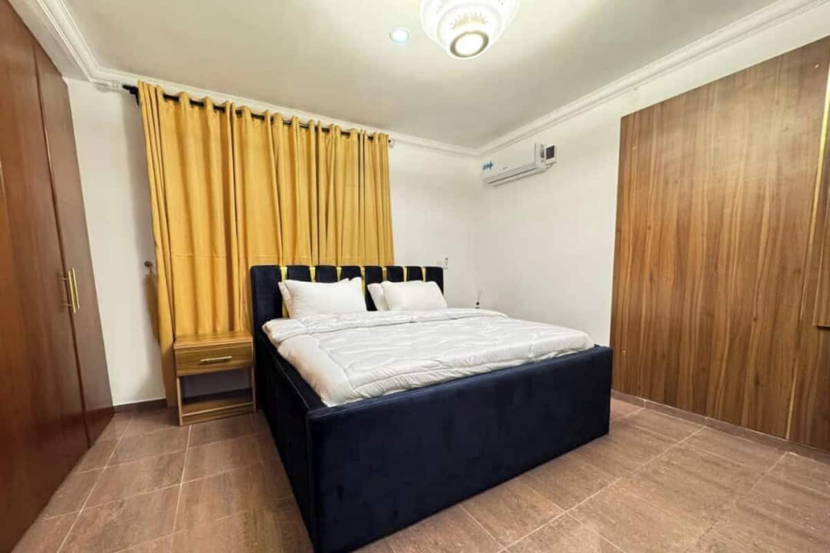 Un dormitorio con cama, cortinas, un armario y un equipo de aire acondicionado.