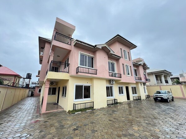 A two-story residential building with a pink and yellow facade, balconies, and a paved driveway. - FRYBURG HOTEL AND SUITES (Lekki)