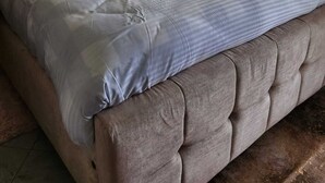 Un letto rifatto con cura, con una testiera capitonata, una coperta a righe e due asciugamani sul letto.