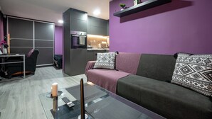 Uma sala moderna com um sofá, uma mesa de centro de vidro e uma área de cozinha ao fundo.